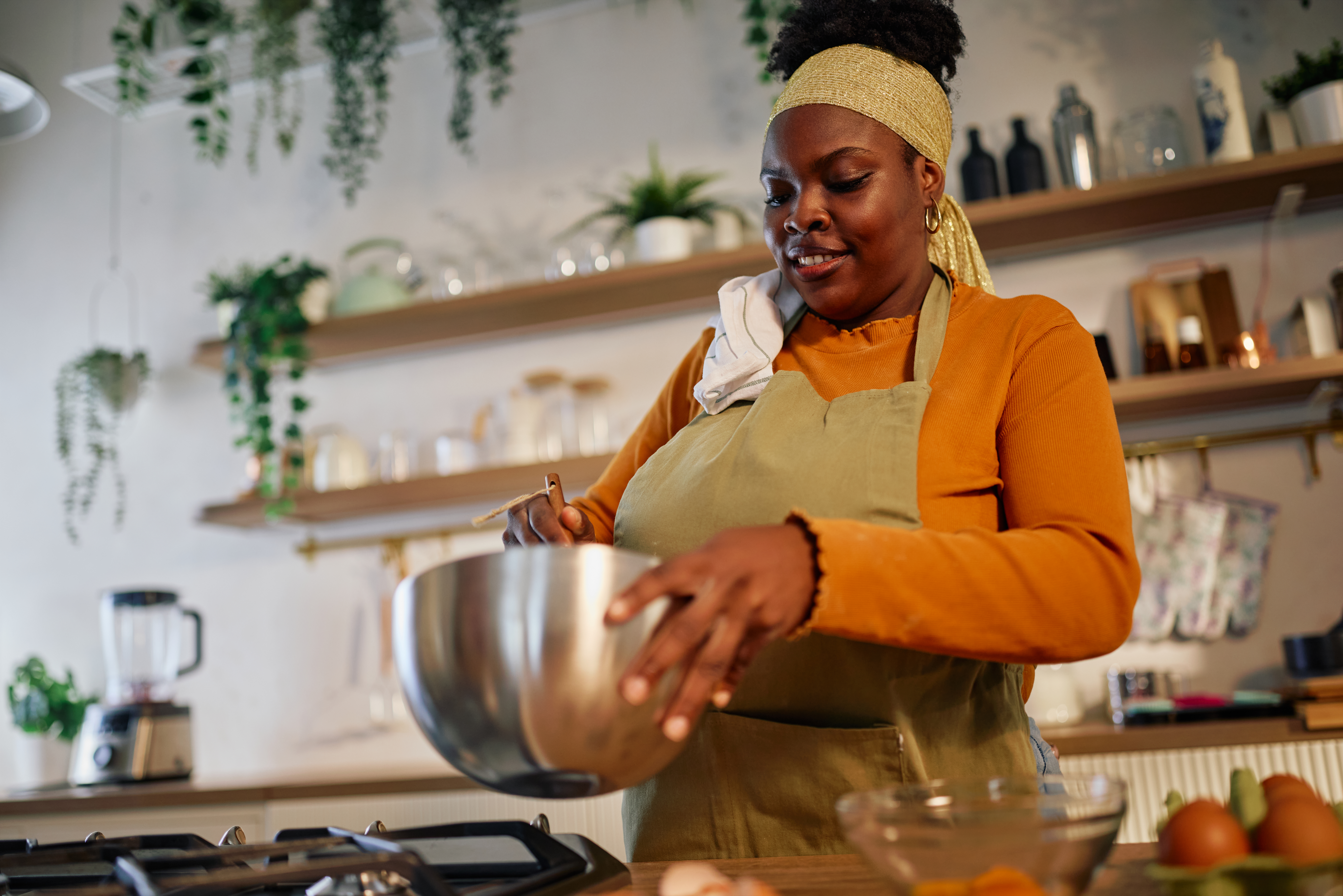 Woman baking at home, preparing food with a bowl and spatula, enjoying cooking hobby in a modern kitchen